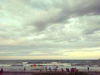 People on beach against cloudy sky