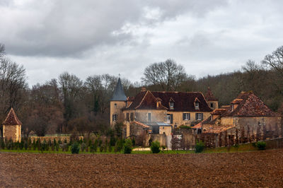 Houses by trees on field against sky