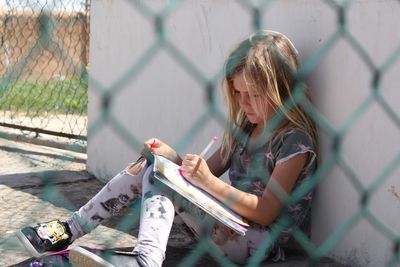 Girl with book seen through chainlink fence