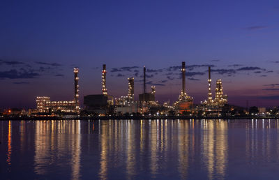 Illuminated factory by river against sky at night