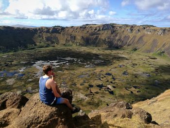 High angle view of hiker looking at view while sitting at crater lake of rano kau