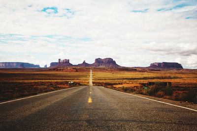 Empty country road by landscape against sky