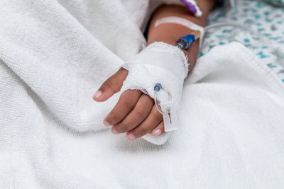 Cropped hand of woman with iv drip on bed at hospital