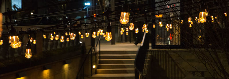Illuminated lights on footpath by building at night