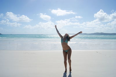 Young woman with arms outstretched standing at beach against sky