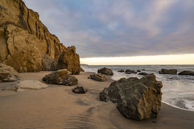 Rocks on beach against sky during sunset