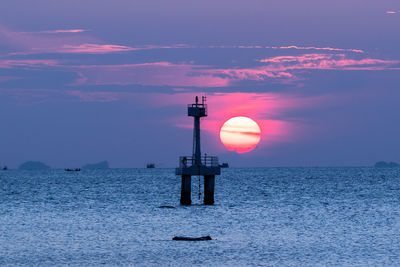 Lighthouse by sea against sky during sunset
