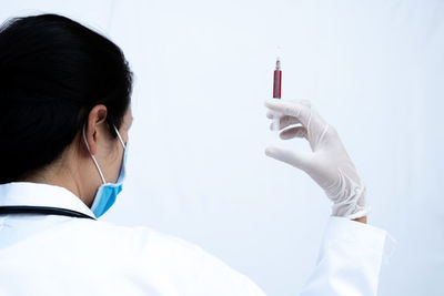 Rear view of doctor holding syringe against white background