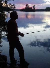 Silhouette man fishing in lake against sky