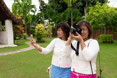 Young woman photographing with mobile phone while standing on plants