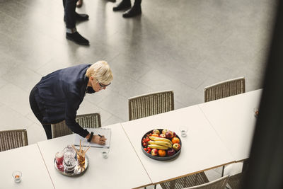 Businesswoman talking on mobile phone and writing in book at office cafeteria