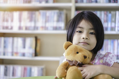 Portrait of girl with teddy bear sitting in library