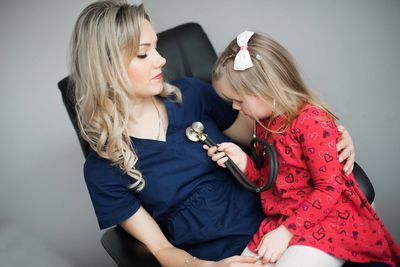 Girl with female doctor holding stethoscope on chair at clinic