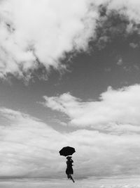 Low angle view of woman holding umbrella while levitating against cloudy sky