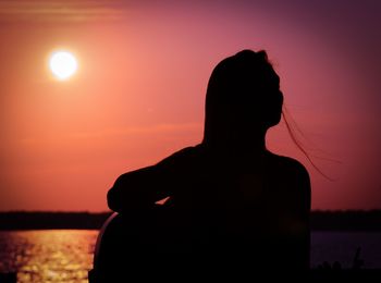 Rear view of silhouette woman standing against sea during sunset