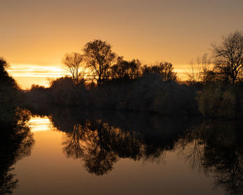 Silhouette trees by lake against sky during sunset