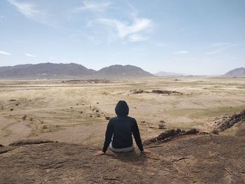 Rear view of man sitting on hill against sky