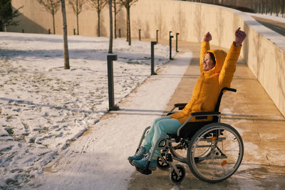 Happy woman in wheelchair happily pulls her hands up while walking in winter park