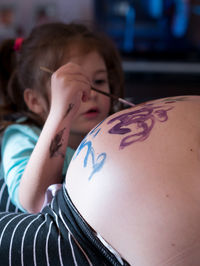 Girl painting pregnant mother belly at home