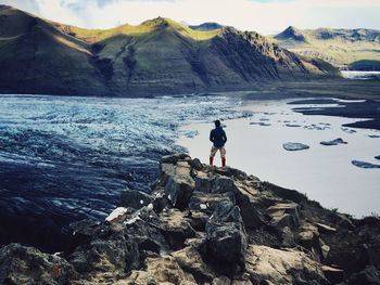 Rear view of woman standing on rock by lake