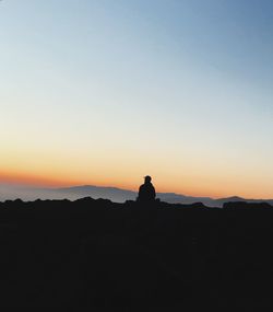 Silhouette man sitting on rock against orange sky