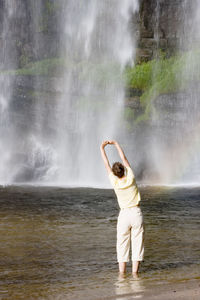 Woman doing gymnastics in front of a tropical waterfall