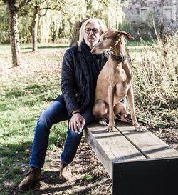 Portrait of senior man sitting with dog on bench at park