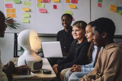 Smiling multiracial students looking at illuminated modern robot in innovation lab