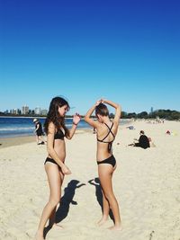 Friends standing on beach against clear sky