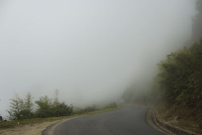 Empty road amidst trees against sky