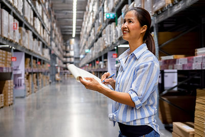 Woman writing while standing in warehouse