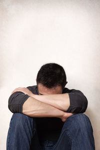 Depressed man sitting against wall