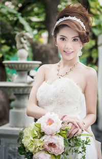 Portrait of smiling bride with bouquet standing outdoors