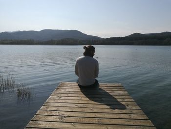 Rear view of man sitting on pier against lake