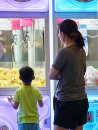 Rear view of mother and son standing by toy store