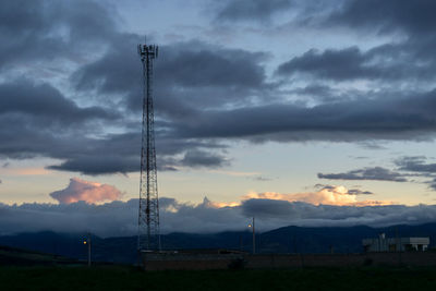 Silhouette electricity pylon on field against sky at sunset