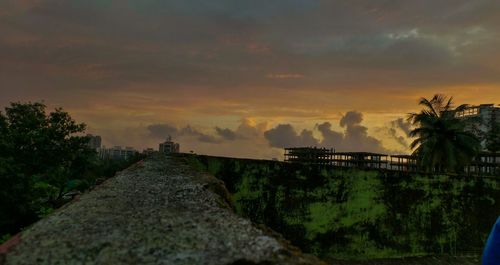Footpath leading towards sea against cloudy sky during sunset