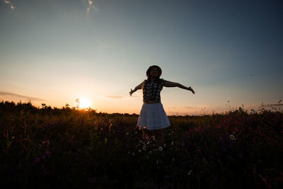 Woman standing on field against sky during sunset