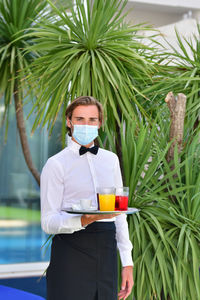 Portrait of waiter holding juice against plants