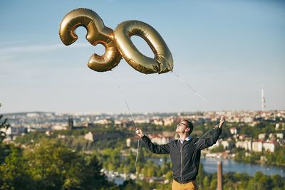 Man holding number 30 helium balloons against cityscape