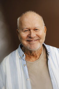 Portrait of smiling elderly man against brown background