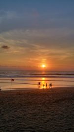 Silhouette people standing on beach against sky during sunset