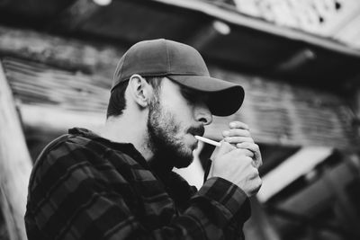 Low angle view of man wearing cap lighting cigarette outdoors
