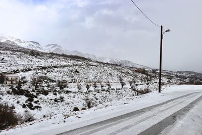 Snow covered road by mountain against sky