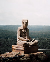 Statue of man sitting on rock against sky