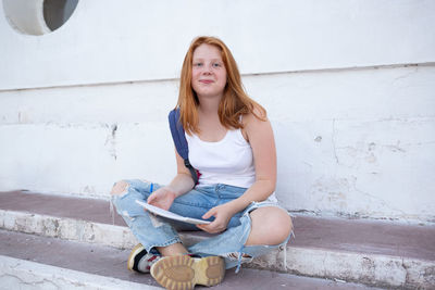 Portrait of young woman sitting against wall