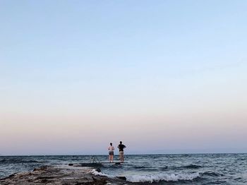 Couple standing at beach against sky during sunset