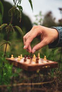 Cropped hand of person playing chess amidst plants