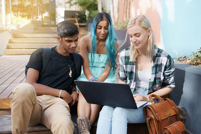 Friends using laptop while sitting outdoors