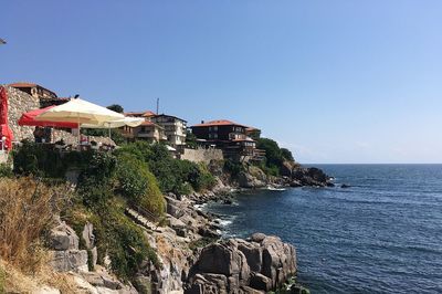 Buildings by sea against clear blue sky